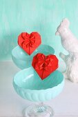 Red origami hearts in turquoise dessert bowls next to china bird