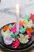 Bunte kleine Origami-Blumen auf schwarzen Tellern mit einer Kerze