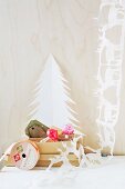 White hand-made paper garland of reindeer next to paper Christmas tree and toadstool ornaments in cardboard box
