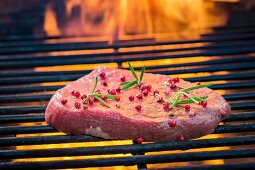 A fresh steak with pepper and rosemery on a grill rack with fire