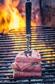 Steaks on a meat fork on a barbecue with rosemary and pepper