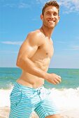 A young man wearing striped bathing trunks and jogging on the beach