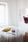 Romantic white lace curtain over bed with blankets and scatter cushions