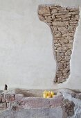 Rendered wall with section of exposed stone masonry, stone trough and candles