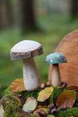 Two wooden toadstools, moss, leaves and acorns in woods