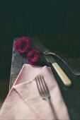 Still-life arrangement of cutlery, pink napkin and roses