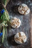 Healthy wholemeal buns with ears of oat and field flowers on a wooden board