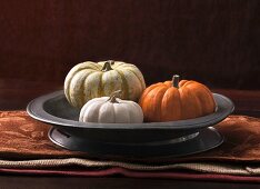An arrangement of three decorative pumpkins in a grey metal dish