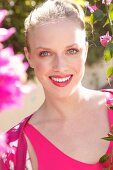 Blonde Frau in pinkfarbenem Top und Cardigan hinter Blumenstrauch