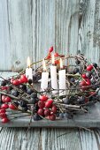 Four lit candles in wreath of sloe branches and rose hips