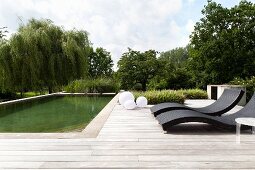 Designer sun loungers on wooden deck adjoining pool
