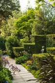 Weg durch sommerlichen Formgarten mit stufenförmiger Hecke