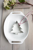 A Christmas tree cutter and a ribbon in an enamel baking dish
