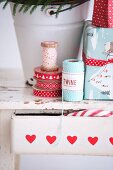 Geschenkbänder, Garnrolle und verpackte Weihnachtsgeschenke auf Holzhocker mit Schublade