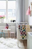 Crocheted patchwork blanket on white cot and small table and chairs in girl's bedroom