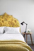 Hocker neben dem Bett mit gelb gepolstertem Betthaupt