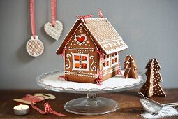 A gingerbread house on a cake stand, decorated with icing