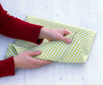 Folding a green and white checked cloth napkin (2/5)