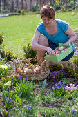 Frau füllt Osternest im Blumenbeet mit bunten Ostereiern