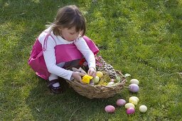 Girl with Easter nest on the lawn sticks narcissus flower to Easter bunny