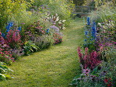 Lawn path between beds with perennials, summer flowers and grasses