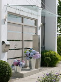 Modern house entrance with glass canopy, tubs with hydrangeas