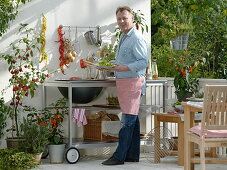 Outdoor-Küche auf dem Balkon: Mann grillt Paprika, Töpfe mit Glockenchili