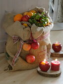 Korb mit Äpfeln (Malus) und Orangen (Citrus sinensis) im Jutesack