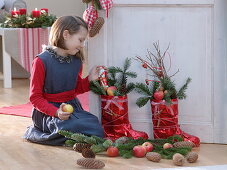 Girl next to red Father Christmas boots, filled with Abies (fir), apples