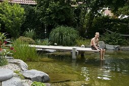 Swimming pond with wooden footbridge bordered with granite blocks