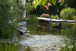 Swimming pond with wooden footbridge bordered with granite blocks