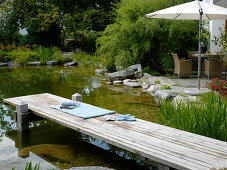 Swimming pond with wooden footbridge bordered with granite blocks