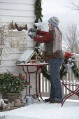 Winter balcony with conifers, bird feeder house, snow and garland