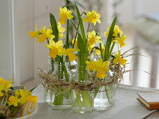 Narcissus 'Tete a Tete' (Narcissus), small bottles as vases in a straw wreath