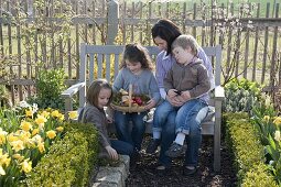 Woman with children in the garden on the bench, chip basket as Easter nest