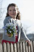 Girl behind fence with bouquet of Myosotis (Forget-me-not)