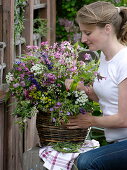 Woman puts a bouquet of meadow flowers in a wicker vase