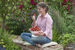 Young woman sitting on a wall and eating freshly picked strawberries