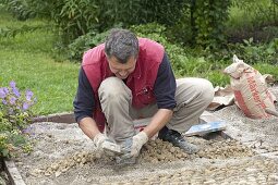 Mann legt Pflaster aus Kieselsteinen (Mittelkorn-Größe) in Riesel-Zement