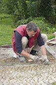 Mann legt Pflaster aus Kieselsteinen (Mittelkorn-Größe) in Riesel-Zement