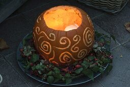 Bright pumpkin (Cucurbita), decoratively carved, in wreath of Hedera