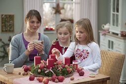 Mutter mit Töchtern bastelt Adventskranz