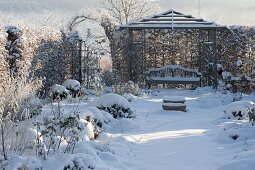 Rose garden with hedge, arbour and bench in the snow