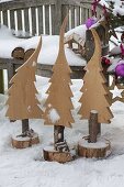 Wooden fir trees in tree slices in front of bench, bird feeder house