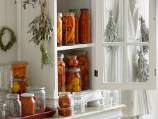 Small cupboard with preserved tomatoes in vinegar, chilli peppers and tomato sugo