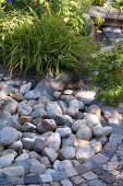 Stream made of paving stones between Hemerocallis (daylilies), Geranium