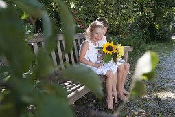 Children with Helianthus (sunflowers) on a wooden bench under an apple tree