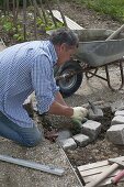 Mann legt Abrundung der Beet-Einfassung aus Granit-Steinen