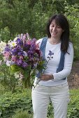 Frau im Garten mit Strauß aus Aquilegia (Akelei), Syringa (Flieder)