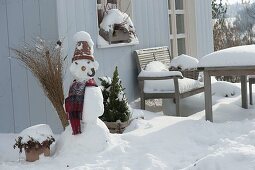 Snowman with clay pot as hat, scarf, cabbage stump as pipe, carrot as nose